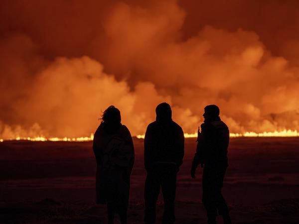 Menschen beobachten, wie der Nachthimmel nach dem Ausbruch des Vulkans erleuchtet wird.
