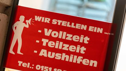 Ein rotes Schild mit der Aufschrift ·Wir stellen ein - Vollzeit, Teilzeit, Aushilfen· hängt am Eingang einer Bäckerei in der Innenstadt von München. 