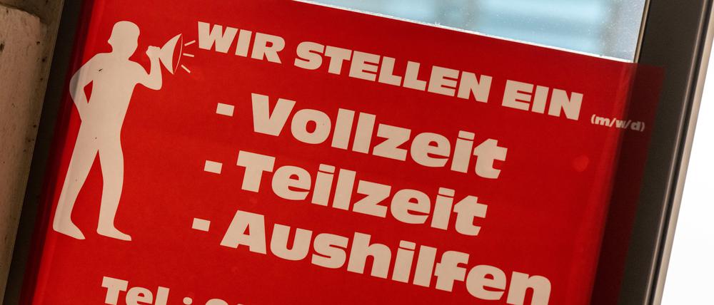 Ein rotes Schild mit der Aufschrift ·Wir stellen ein - Vollzeit, Teilzeit, Aushilfen· hängt am Eingang einer Bäckerei in der Innenstadt von München. 
