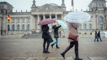 Touristen halten bei nasskaltem Wetter Regenschirme in den Händen und gehen am Reichstagsgebäude vorbei.
