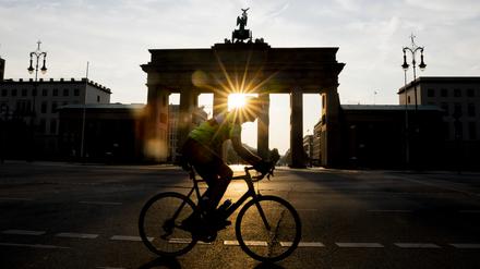 Ein Radfahrer fährt bei aufgehender Sonne am Brandenburger Tor vorbei.
