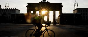 Ein Radfahrer fährt bei aufgehender Sonne am Brandenburger Tor vorbei.