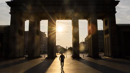 Ein Mann läuft bei aufgehender Sonne durch das Brandenburger Tor.