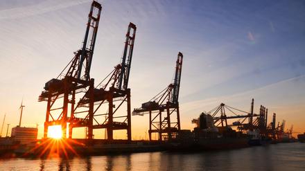 Die Sonne geht hinter Containerbrücken auf dem Terminal Eurogate im Waltershofer Hafen in Hamburg unter. 