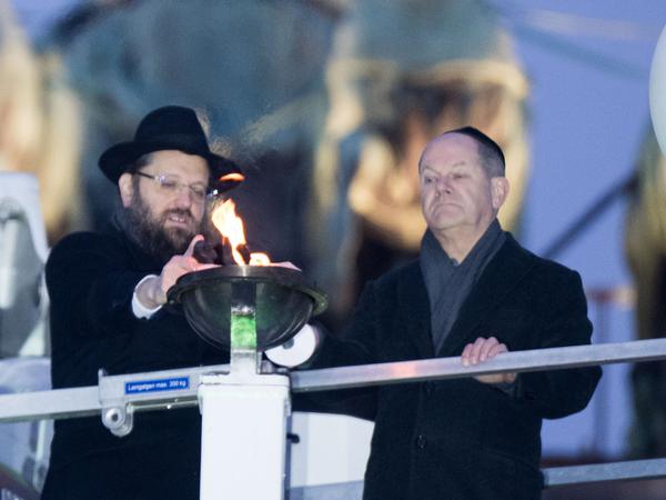 Rabbiner Yehuda Teichtal (l) und Bundeskanzler Olaf Scholz (SPD) zünden beim traditionellen zentralen Chanukka-Lichterzünden am Brandenburger Tor das mittlere Licht an. 