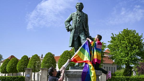 Am Denkmal von Kronprinz Friedrich zeigen der Politiker Freke Over und Marie von der Vorbereitungsgruppe des ersten „Christopher Street Day“ (CSD) in Rheinsberg die Regenbogenfahne.