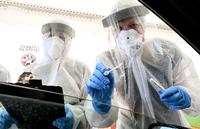 Mitarbeiter vom Gesundheitsamt in Mitte halten ein Abstrichstäbchen in ein Autofenster auf dem zentralen Festplatz in der ambulanten Corona-Test- Einrichtung.