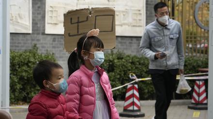 Kinder mit Masken gehen an einem Schild mit der Aufschrift „Ausgang“ an einer COVID-Teststation in Peking vorbei.