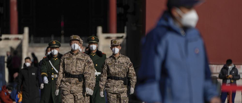 Soldaten und paramilitärische Polizisten mit Mund-Nasen-Schutz marschieren durch maskierte Besucher in der Verbotenen Stadt.