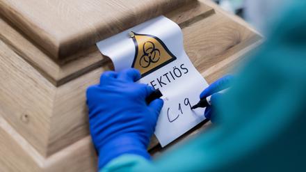 Ein Bestattungsunternehmer schreibt „C19“ auf ein Schild mit dem Hinweis „Infektiös“ an einem Sarg mit einem Verstorbenen.