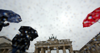 Bei Regen gehen Touristen vor dem Brandenburger Tor in Berlin vorbei.