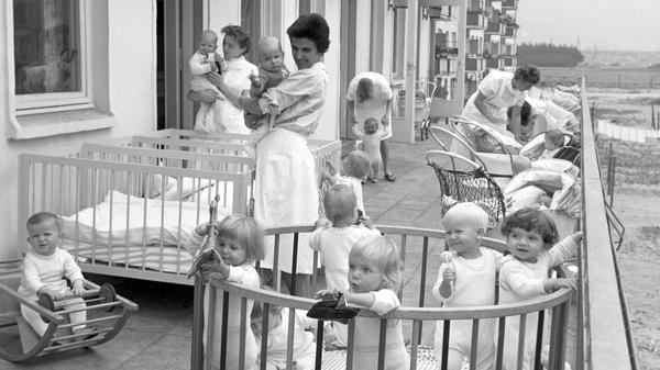 In der Neustadt von Hoyerswerda sind 1963 die Kleinen aus einer Kinderkrippe mit ihren Erzieherinnen auf der Terrasse.