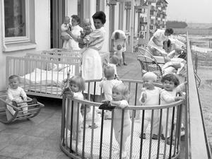 In der Neustadt von Hoyerswerda sind 1963 die Kleinen aus einer Kinderkrippe mit ihren Erzieherinnen auf der Terrasse.