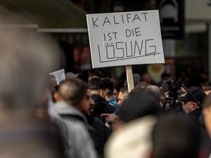 Teilnehmer einer Islamisten-Demo halten ein Plakat mit der Aufschrift „Kalifat ist die Lösung“ in die Höhe. 