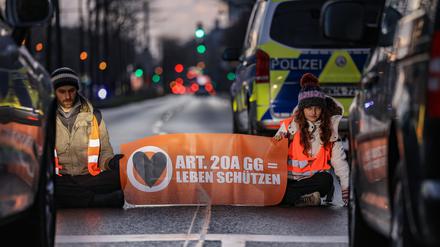 Aktivisten der Umweltschutzorganisation Letzte Generation sitzen vor Fahrzeugen auf einer Straße in Köln. 