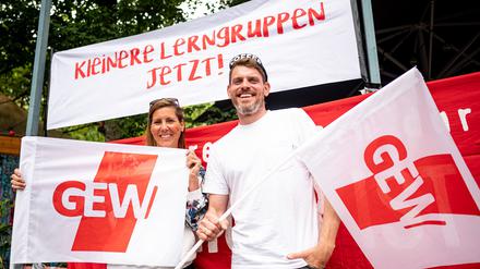 Sven und Bianca, beide Lehrer an einer Neuköllner Schule, stehen mit zwei GEW-Flaggen beim Warnstreiks an den Berliner Schulen in Berlin-Kreuzberg vor einem Banner mit der Aufschrift „Kleinere Lerngruppen jetzt!“.