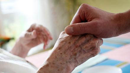 Ein Pfleger hält in einem Pflegeheim die Hand einer Bewohnerin. 