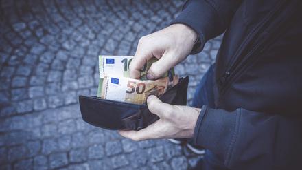 Ein Mann öffnet seine Geldbörse und hält 150 Euro Geldscheine in seiner Hand. Mann mit Bargeld in der Hand