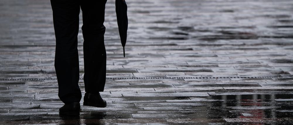 Ein Passant geht mit einem Regenschirm in der Hand durch eine Fußgängerzone.