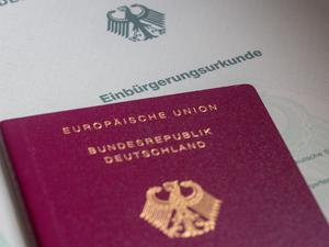 Eine Einbürgerungsurkunde der Bundesrepublik Deutschland und ein deutscher Reisepass liegen auf einem Tisch. 