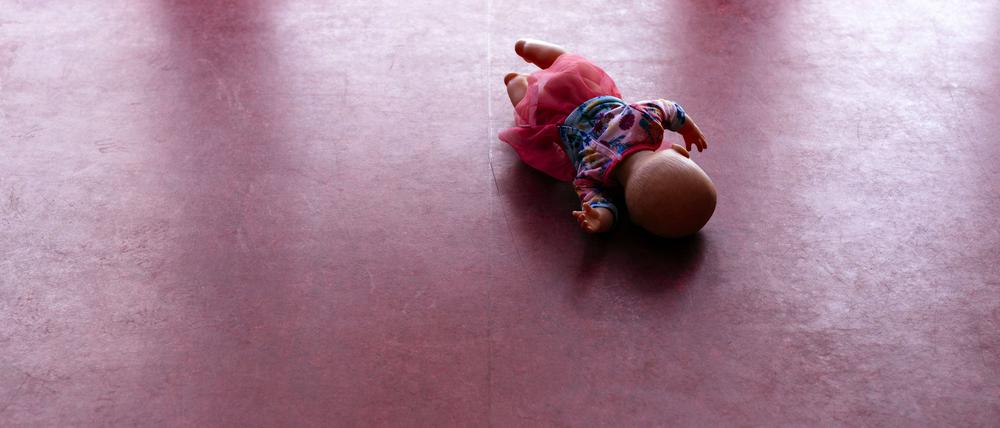 Eine Spielzeugpuppe liegt auf einem PVC-Fußboden. 