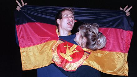 Ein jubelnden Paar hat sich am 3. Oktober 1990 in einer DDR-Fahne dort Platz geschaffen, wo früher das Emblem Hammer und Sichel war - und feierte frenetisch den historischen Anlass.