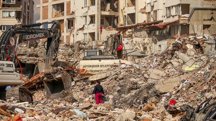 Ein Mann steht zwischen Trümmern, während Bagger die Überreste eines zerstörten Gebäudes einreißen. 