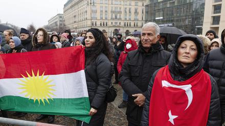 Trauernde haben sich zu einer Gedenkveranstaltung für die Opfer des Erdbebens in der Türkei und Syrien am Brandenburger Tor versammelt und ziegen eine kurdische und eine türkische Flagge. 