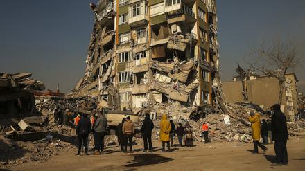 Menschen stehen vor einem halb eingestürzten Gebäude in Kahramanmaras.