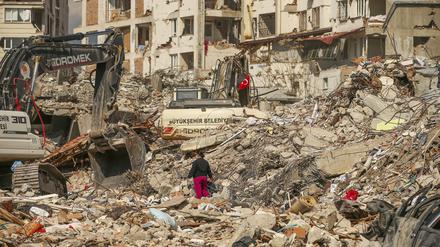Ein Mann steht zwischen Trümmern, während Bagger die Überreste eines zerstörten Gebäudes nach dem Erdbeben am 06.02.2023 abreißen.