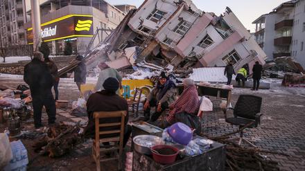 Menschen stehen und sitzen vor eingestürzten Gebäuden in Golbasi. In der Region sollten erdbebensichere Bauten errichtet werden. 