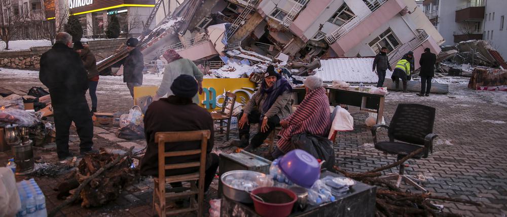 Menschen stehen und sitzen vor eingestürzten Gebäuden in Golbasi. In der Region sollten erdbebensichere Bauten errichtet werden. 