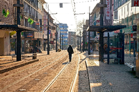 Ein Mann geht durch eine menschleere Fußgängerzone mit Straßenbahngleisen.