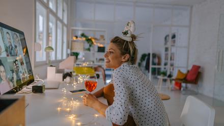 Photo of a young woman celebrating Christmas by having a virtual Christmas party with her friends; drinking wine, celebrating Christmas and holidays apart from friends and family, and practicing social distancing.