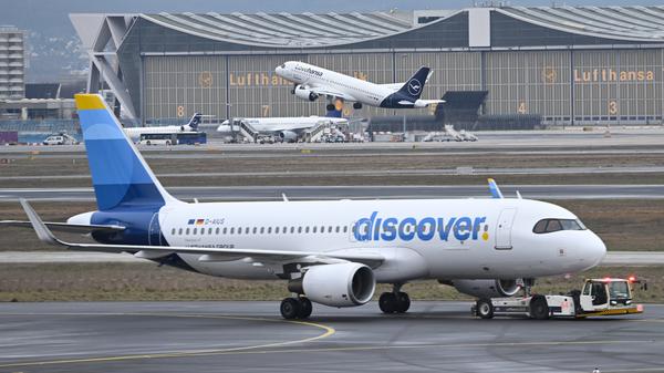 Während eine Maschine der Lufthansa startet, wird ein Passagierflugzeug der Discover Airlines am Frankfurter Flughafen von einem Schlepper gezogen. 