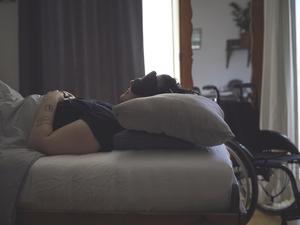 Eine Frau mit ME/CFS liegt mit Schlafmaske in einem abgedunkelten Zimmer. (Symbolbild)