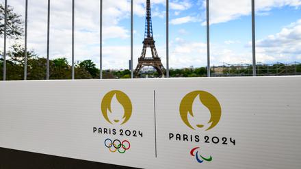 Die Olympischen Ringe und das Logo der Paralympischen Spiele sind auf einem Schild an einem Bauzaun vor dem Eiffelturm zu sehen.