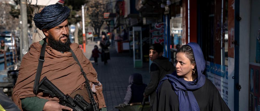 Ein Taliban-Kämpfer steht in Kabul in Afghanistan Wache, während eine Frau vorbeiläuft (Symbolbild). 