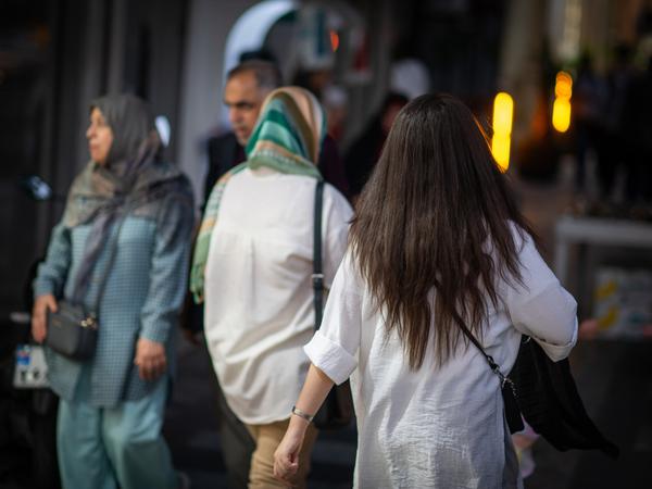 En kvinne går nedover en gate i Teheran med håret ned om kvelden, med to kvinner med hodesjal i bakgrunnen (symbolsk bilde).