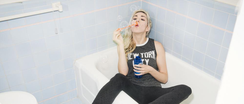 Fully clothed young woman blowing bubbles in bathtub