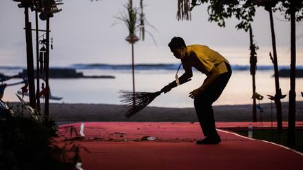 Ein Mann kehrt am Morgen beim G20-Gipfel einen roten Teppich am Strand. 
