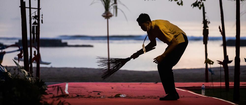 Ein Mann kehrt am Morgen beim G20-Gipfel einen roten Teppich am Strand. 