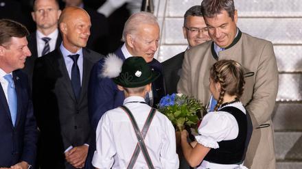 Kinder in Trachten und Marcus Söder begrüßen den US-Präsidenten Joe Biden.