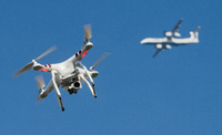 Eine private Drohne fliegt in knapp 10 Metern Flughöhe über einem Garten, als in weiter Entfernung ein Flugzeug beim Anflug auf den Flughafen Düsseldorf zu sehen ist.