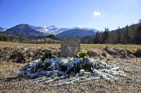 Inmitten von Blumen steht eine steinerne Gedenkstele mit der Aufschrift "In Erinnerung an die Opfer des Flugzeugunglücks vom 24. März 2015" in den vier Sprachen Englisch, Deutsch, Spanisch und Französisch in La Vernet, Frankreich, nahe der Unglücksstelle.