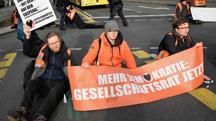 Activists of the environmental group "Last Generation" (Letzte Generation) are glued on the ground with a banner reading "More democracy: Society Council now", while police remove fellow activists (background) during a protest for climate change on April 5, 2023  in Berlin’s Charlottenburg district. (Photo by Tobias SCHWARZ / AFP)