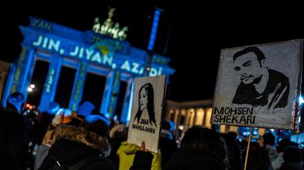 Activists display placards featuring portraits of recently executed Iranian demonstrator Mohsen Shekari (R), and Kurdish woman Mahsa Amini who died in police custody, during a demonstration in support of demonstrators in Iran, in front of the Brandenburg Gate illuminated with the words "Woman, Life, Freedom" in various languages including Kurdish and Persian, in Berlin on December 13, 2022. (Photo by John MACDOUGALL / AFP)