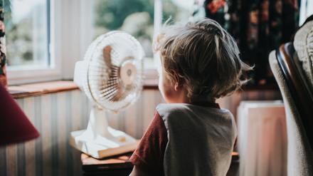 Ein kleiner Junge vor einem Ventilator. Es gibt noch andere Maßnahmen, um Räume kühl zu halten. 