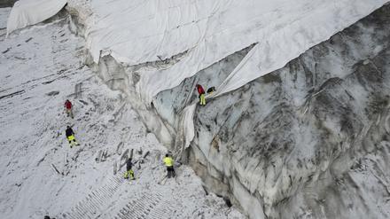 Blick auf den Corvatsch-Gletscher, waehrend Mitarbeiter der Bergbahnen Gletscher-Schutzvlies entfernen.  Glaziologen haben ihr Programm zur Vermessung des Gletschers eingestellt. Die Entscheidung wurde bereits im Jahr 2019 getroffen, doch der heiße Sommer 2022 hat zu «extremen Eisverlusten» und dem Ende des Programms geführt. Der bedeckte Teil des Gletschers wird im Winter als Skipiste genutzt. 