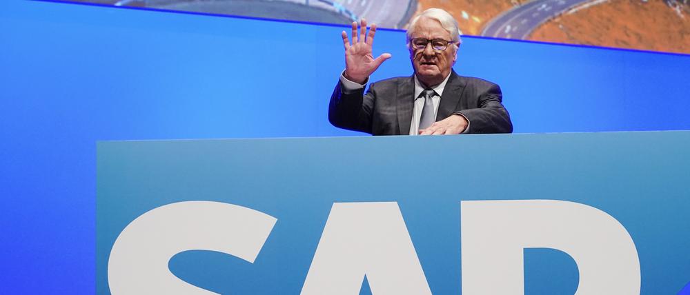 Hasso Plattner steht winkend hinter einer Tafel mit einem großen SAP-Schriftzug.